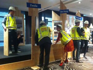 Onder het toeziend oog van een Kamper lid van de Hoogwaterbrigade voegen Hans de Jong (DB-lid van waterschap DODelta voor Water Natuurlijk) en Annemieke Nijhof (CEO van Tauw) een plank in de symbolische waterkering. (9 maart 2016, Werkconferentie IJssel-Vechtdelta)